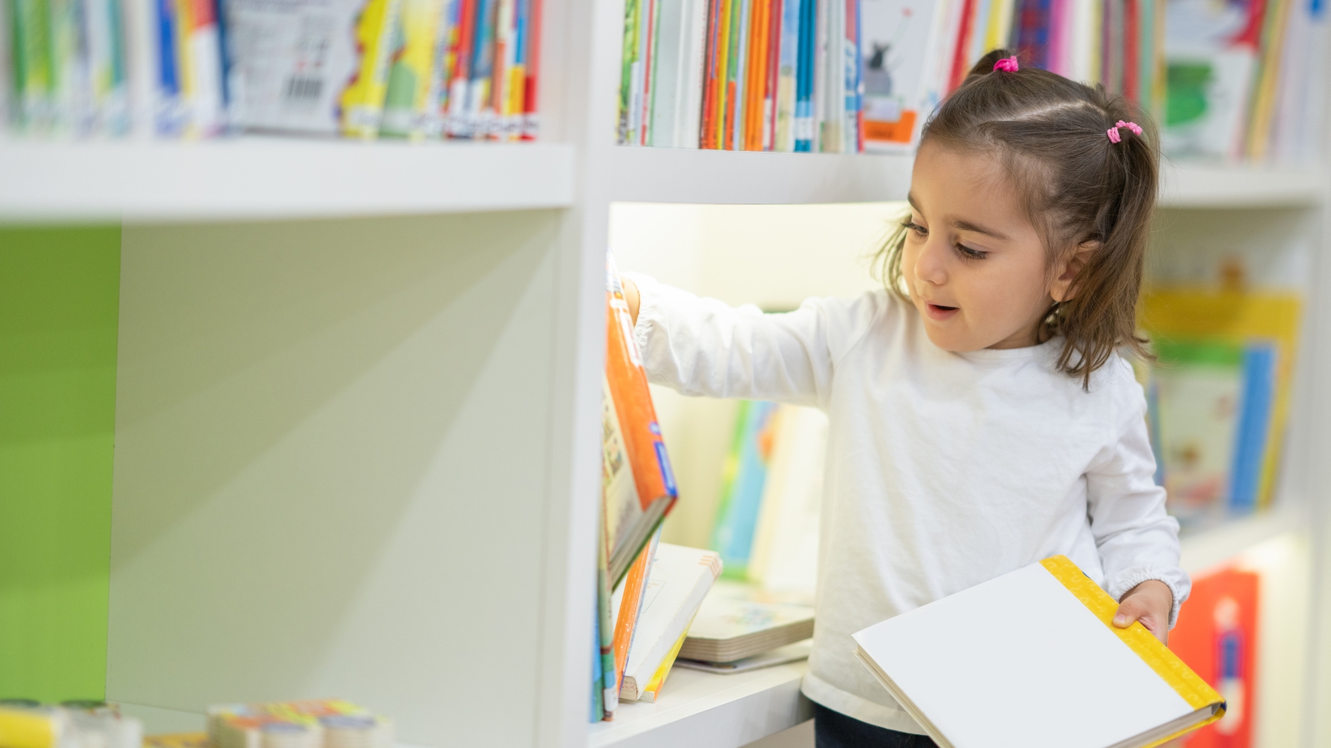 A little girl choosing her own book to read from her shelves via Canva.